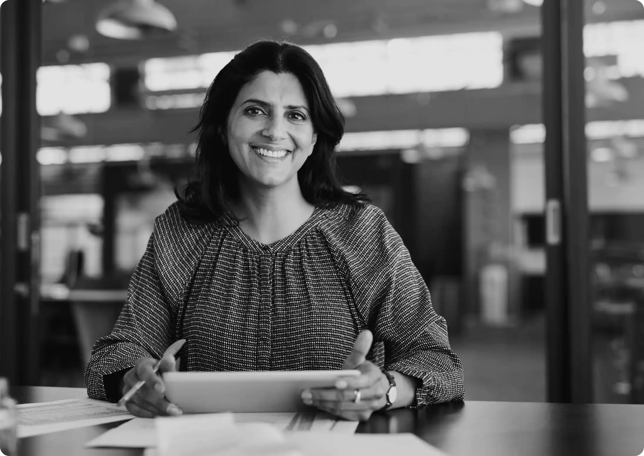 Smiling woman holding a tablet at a desk in an office, representing a satisfied head of cybersecurity human risk management.